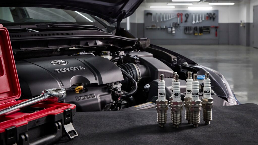 Best spark plugs for Toyota Camry with NGK Iridium plugs displayed beside a Toyota Camry engine